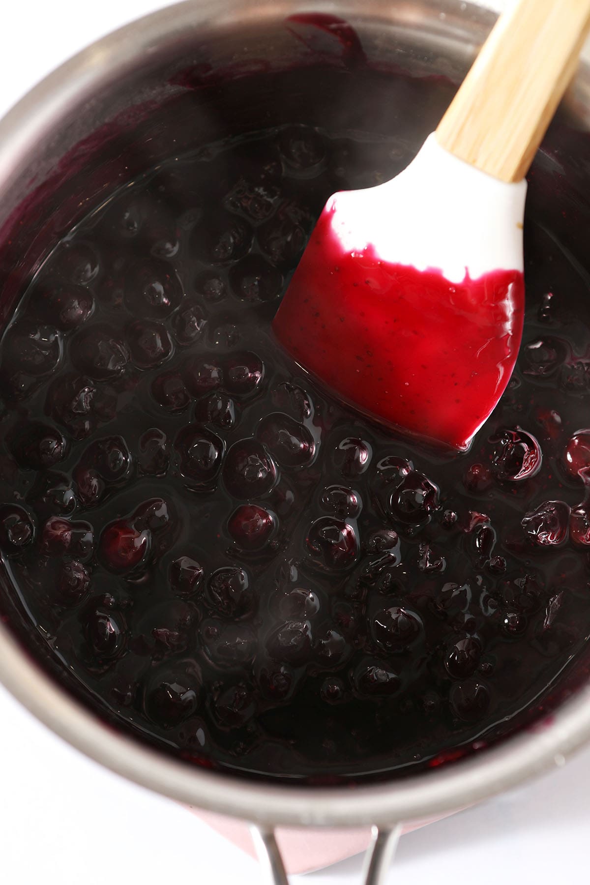 a rubber spatula stirs a blueberry sauce in a saucepan