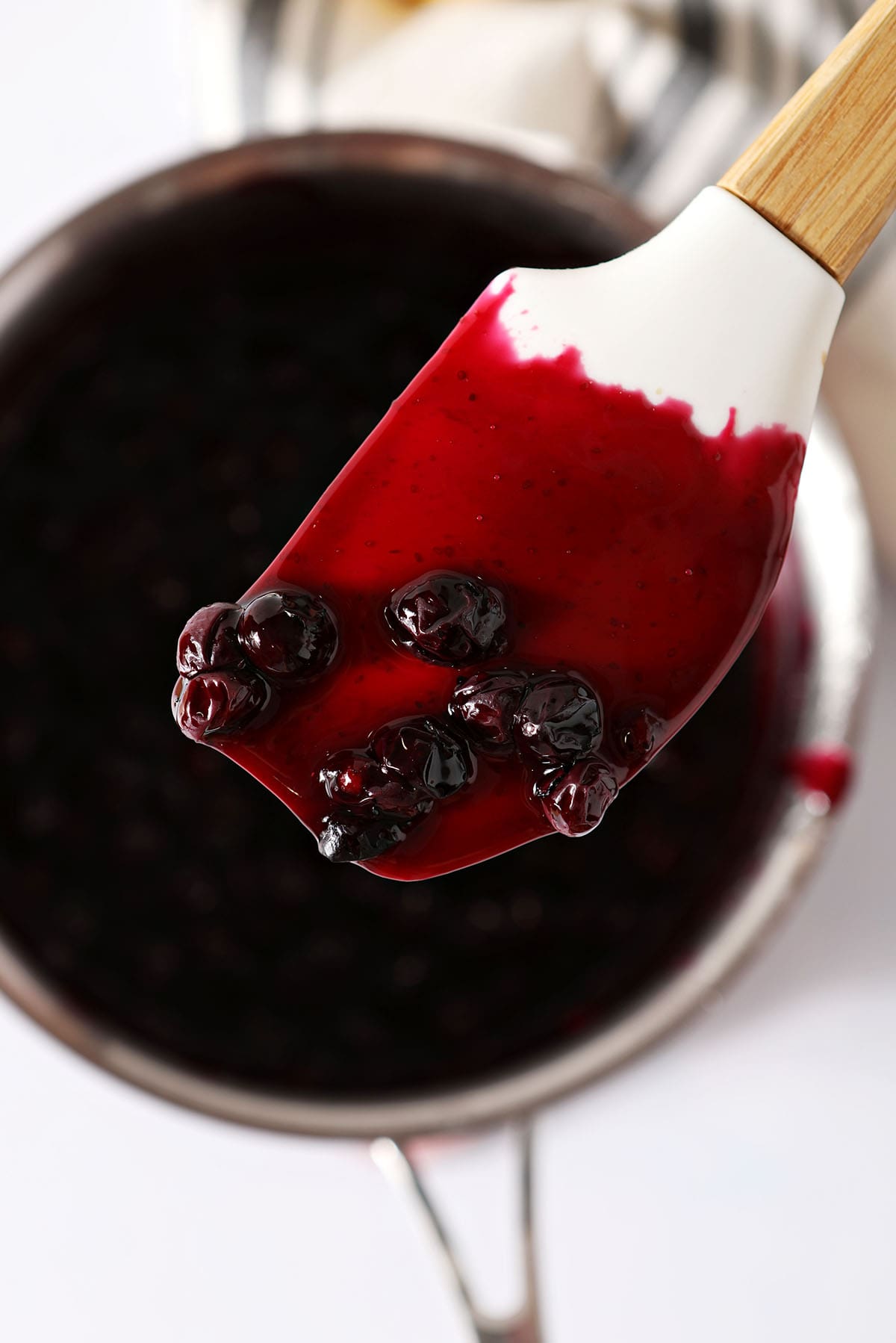 a rubber spatula holds a little blueberry sauce over a saucepan