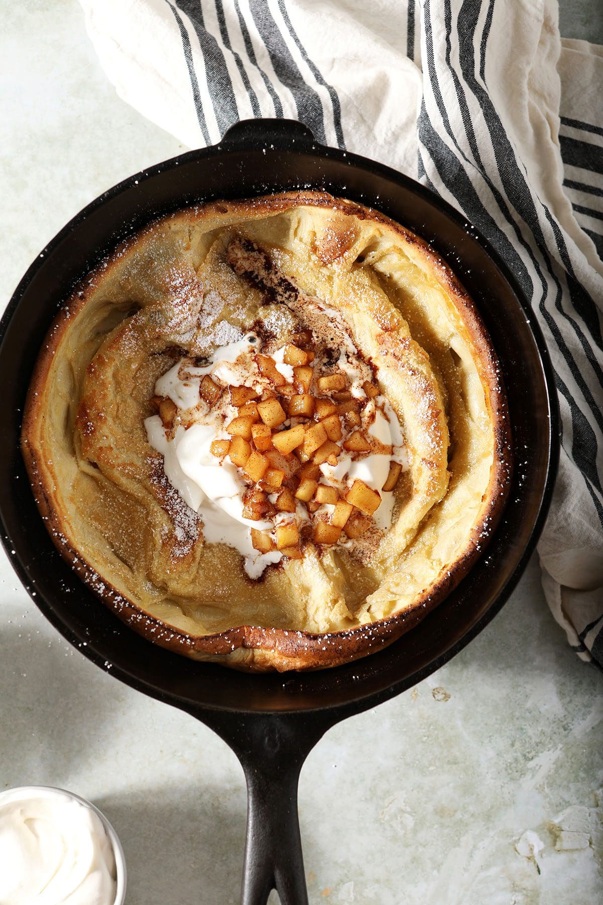 A Dutch pancake with whipped cream and caramelized apples in a skillet