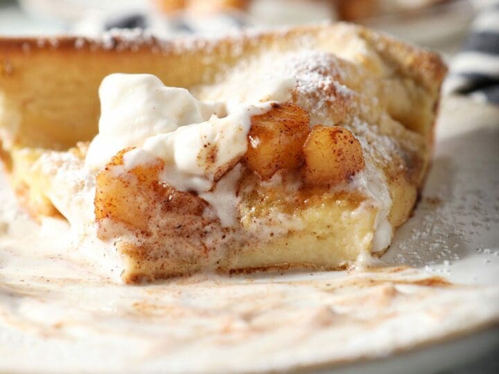Close up of a sliced Dutch baby pancake slice topped with whipped cream and caramelized apples