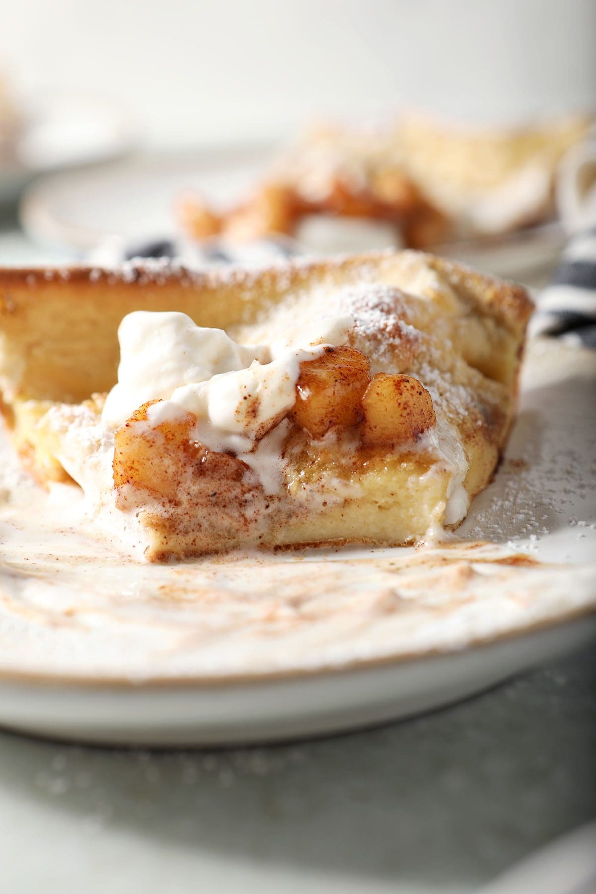 Close up of a sliced Dutch baby pancake slice topped with whipped cream and caramelized apples