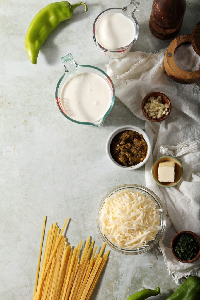 Ingredients to make a spicy Alfredo sauce with green Chile peppers and fettuccine on a green background