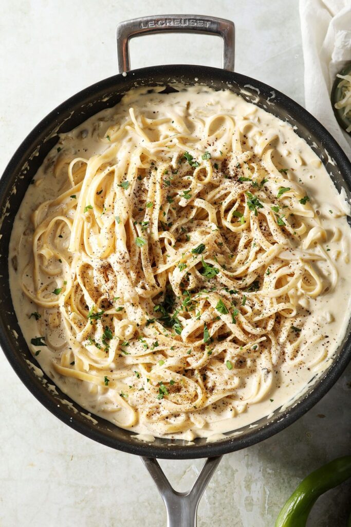 Close up of pasta tossed in a spicy Alfredo sauce topped with black pepper and chopped parsley