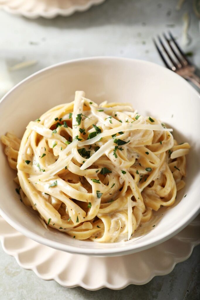 A bowl of spicy fettuccine Alfredo in a white bowl with a fork nearby