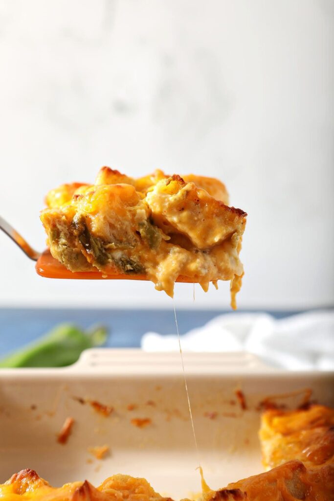 An orange spatula lifts up a slice of egg casserole with green chiles