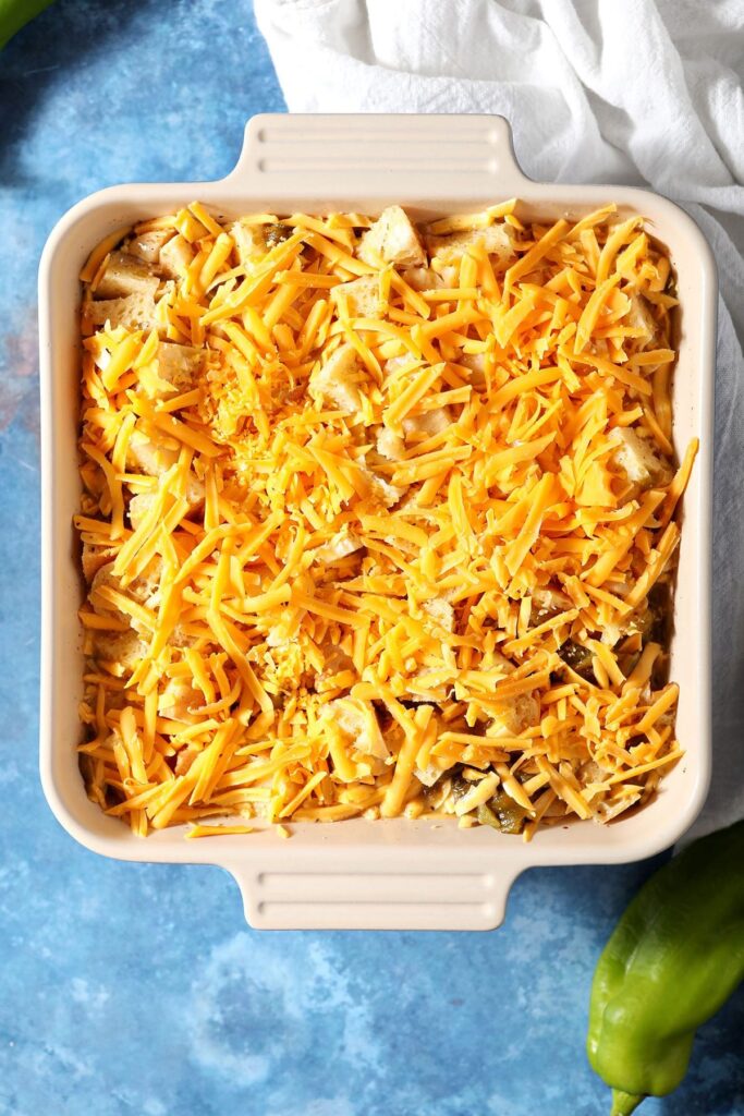 An unbaked egg casserole covered in orange cheese sits on a blue countertop