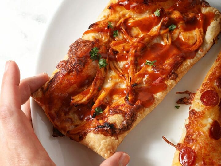 A person grabs a rectangular puff pizza from a platter