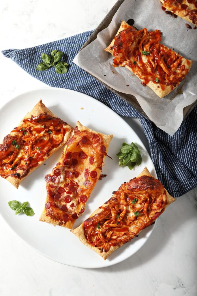 Three puff pastry pizzas on a platter next to a small baking sheet pan with more