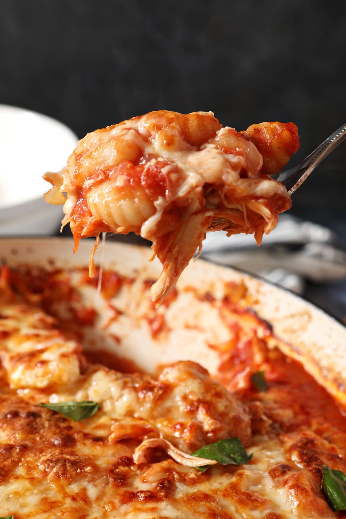 A spoon scoops baked gnocchi from a baking dish