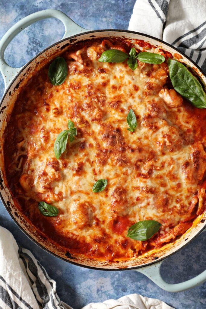 Baked Gnocchi with Chicken in a baking dish on a blue table garnished with fresh basil before serving