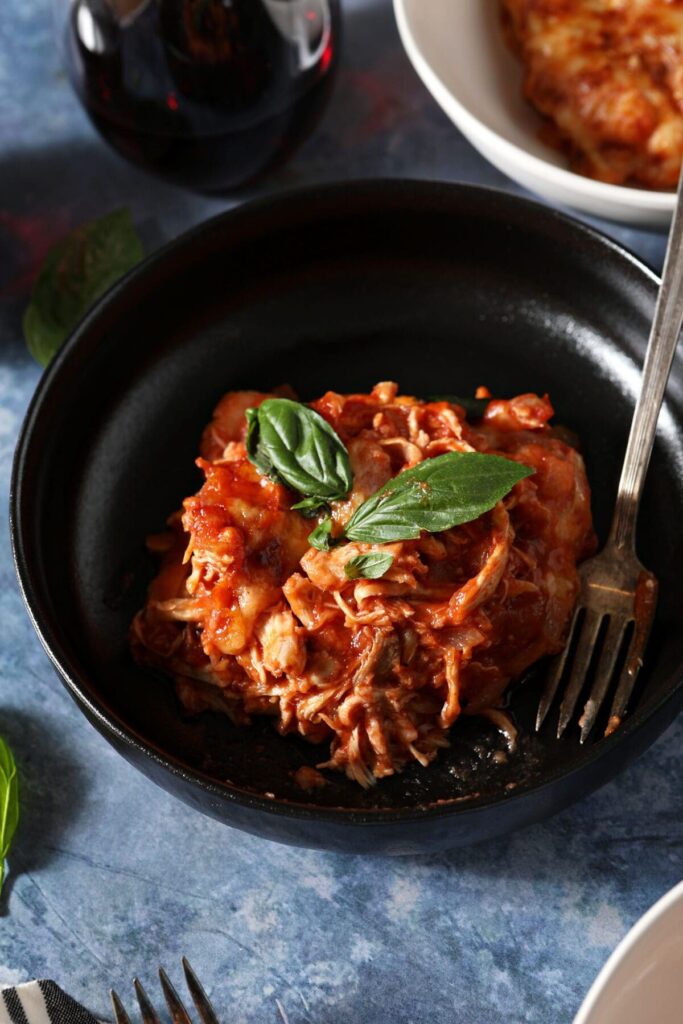 A bowl of a gnocchi bake with chicken with a fork garnished with fresh basil leaves