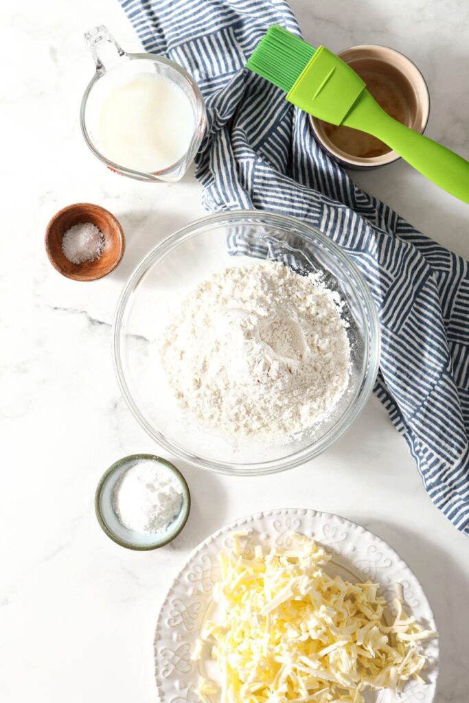 Ingredients to make homemade biscuits in bowls and plates on a marble surface with a blue geometric towel