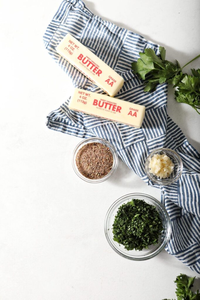 Ingredients to make a compound butter with cajun seasoning on marble with a blue hatched towel and herbs