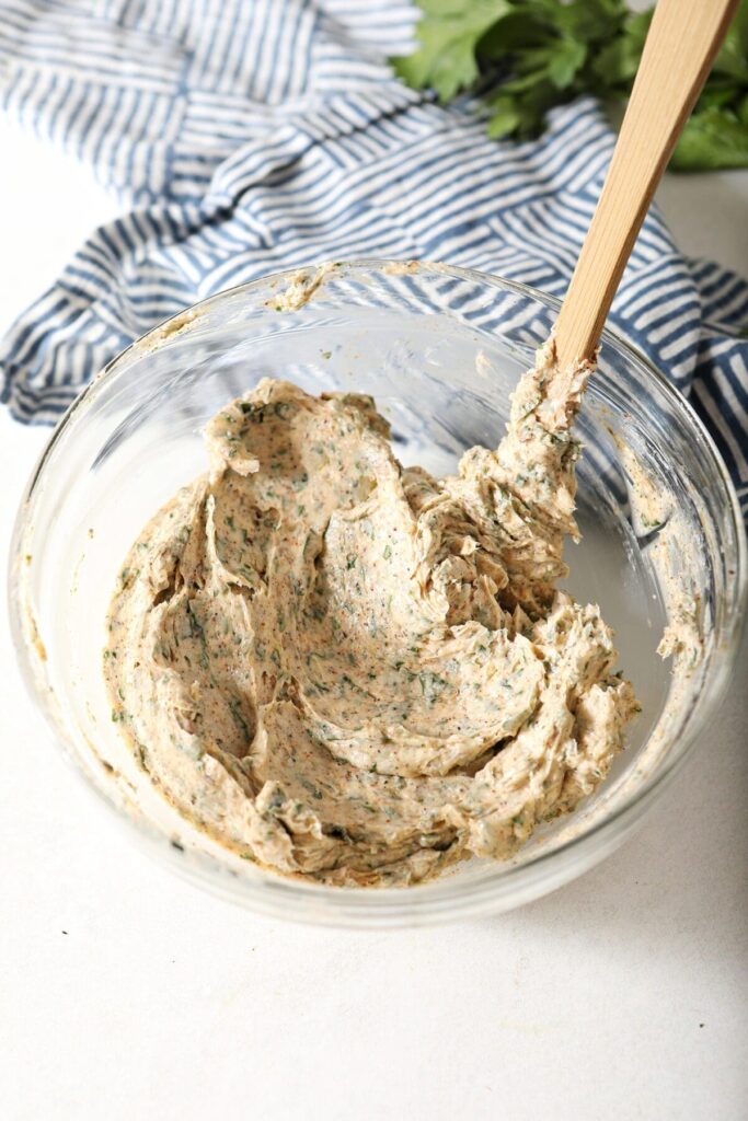 A spatula in a bowl of mixed compound butter on marble