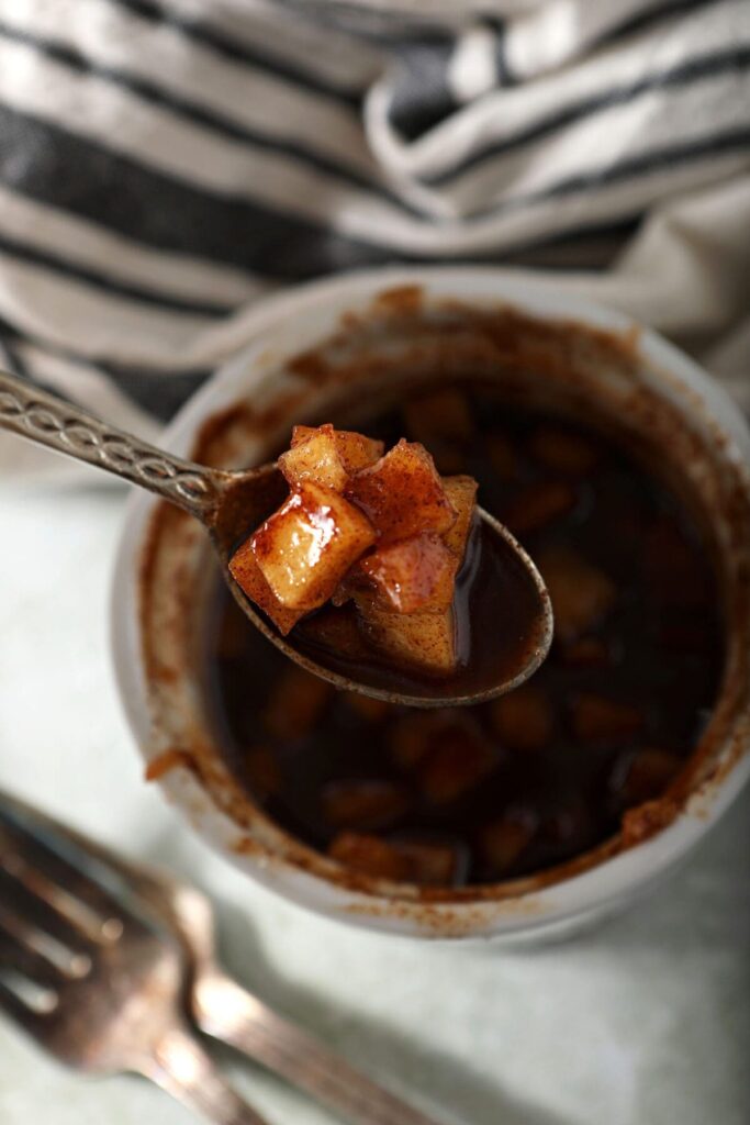 A spoon holds a helping of caramelized apples over a small bowl