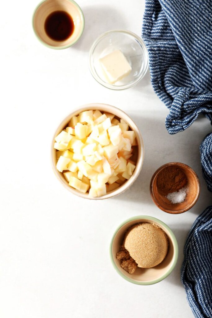 Bowls hold ingredients to make caramelized apples on a marble countertop