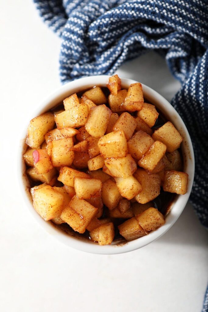 A close up of caramelized apples in a white bowl with a blue striped towel