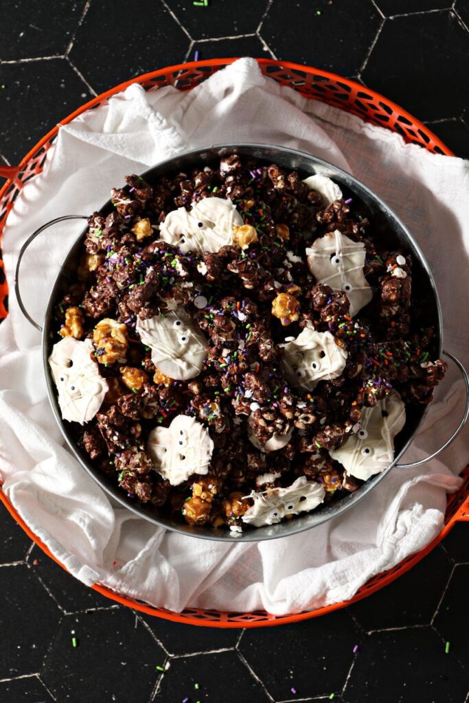 A large bowl of Halloween popcorn snack mix with chocolate, caramel, white chocolate pretzels and sprinkles