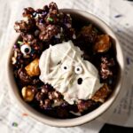 Close up of a white bowl holding Halloween Popcorn Snack mix on top of papers