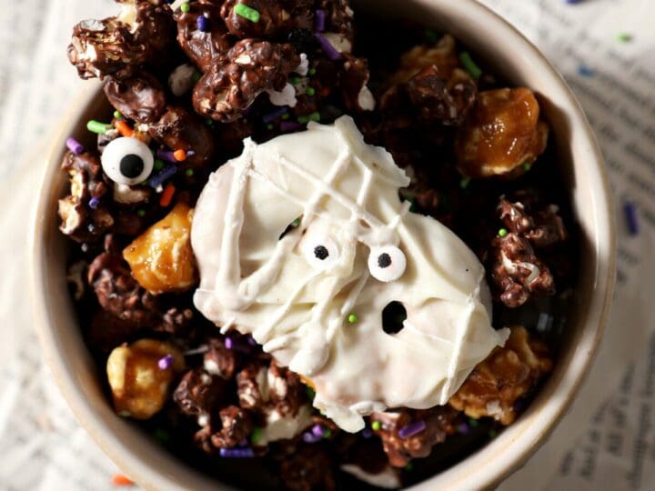 Close up of a white bowl holding Halloween Popcorn Snack mix on top of papers