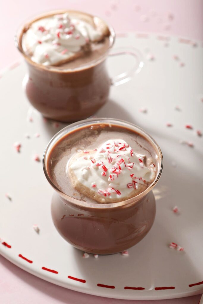 Two mugs of Peppermint Schnapps Hot Chocolate garnished with whipped cream and crushed peppermint on a white tray