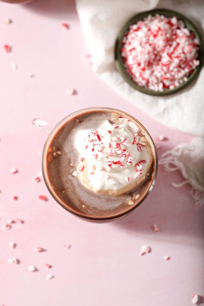 Whipped cream and crushed candy cane on top of a boozy hot cocoa on a pink surface