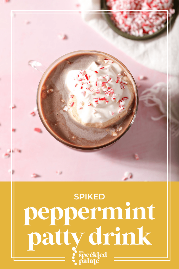 A mug of hot cocoa garnished with whipped cream and peppermint on a pink surface with the text spiked peppermint patty drink