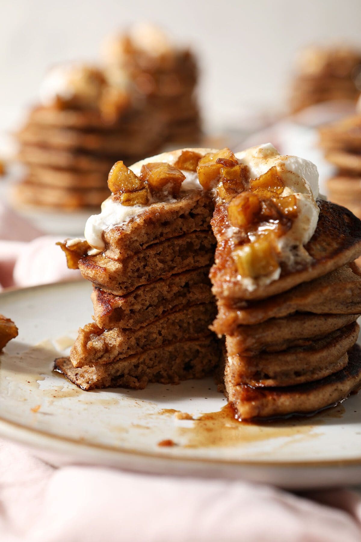 A cut-into stack of Apple Cinnamon Pancakes on a plate garnished with caramelized apples, whipped cream and syrup