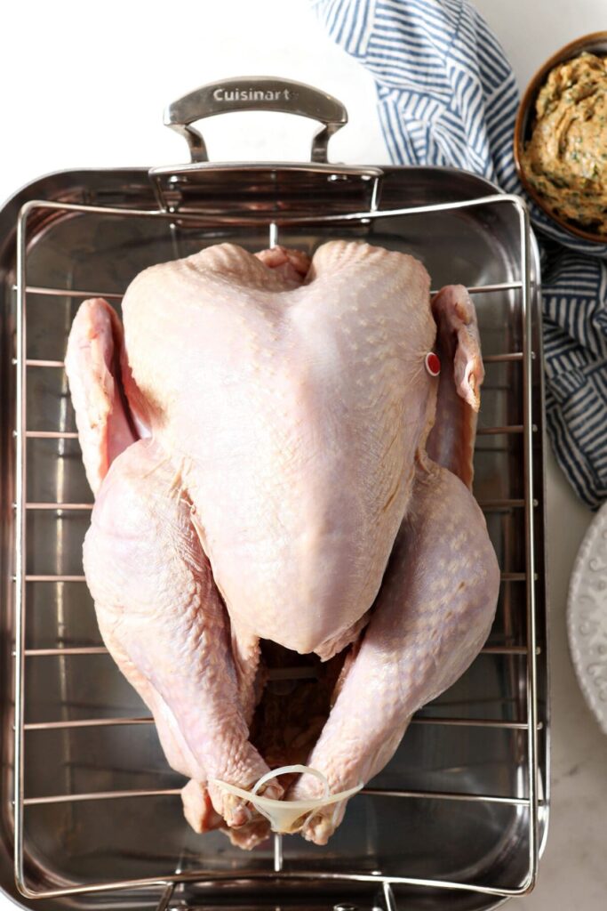 A raw turkey on a roasting pan next to cajun butter