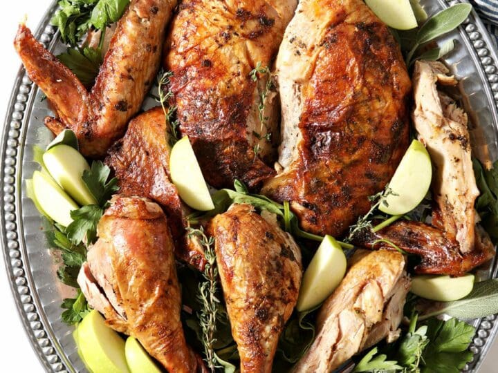 Broken down cooked Cajun Turkey on a silver platter with greens and apples