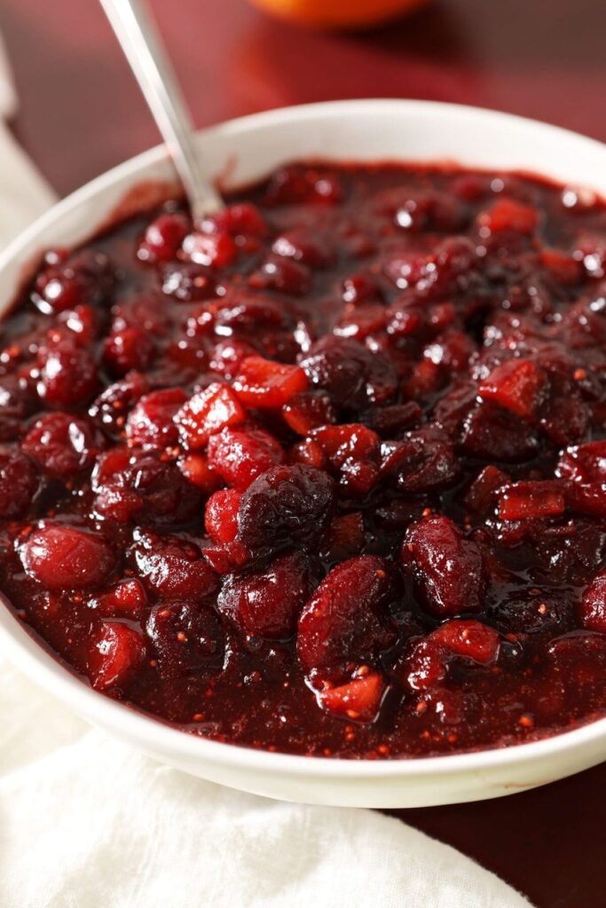 A bowl of spiced cranberry chutney on a red counter with a white napkin