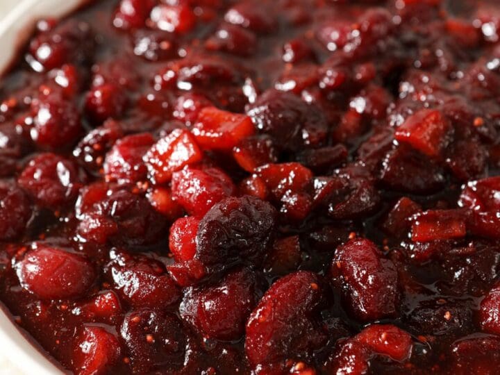 A bowl of spiced cranberry chutney on a red counter with a white napkin
