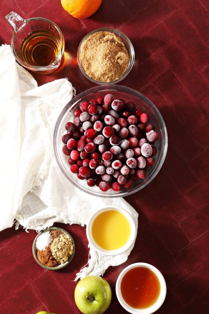 Ingredients to make Cranberry Apple Chutney recipe in bowls on a red countertop with a white towel