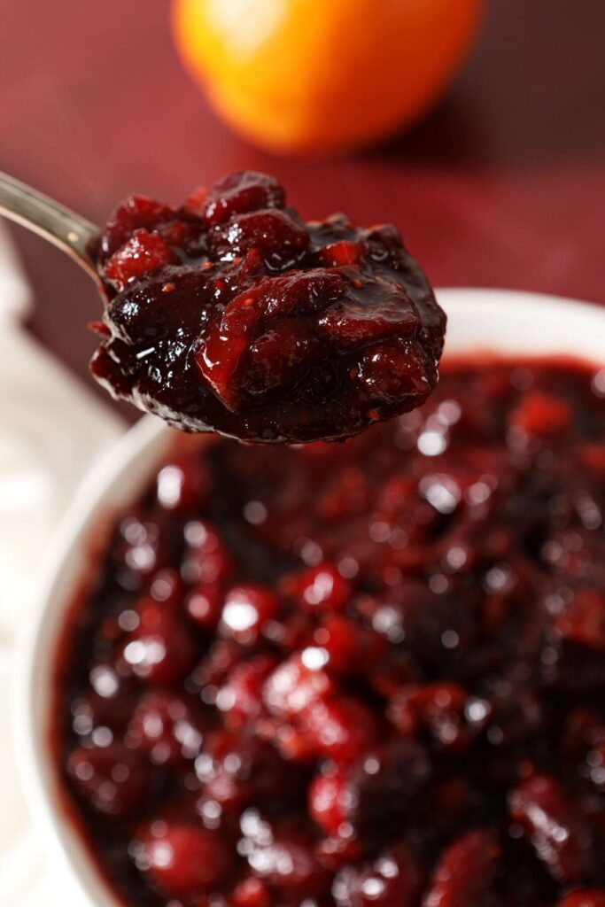 A spoon holds a serving of Spiced Cranberry Apple Chutney above a bowl sitting on a red countertop