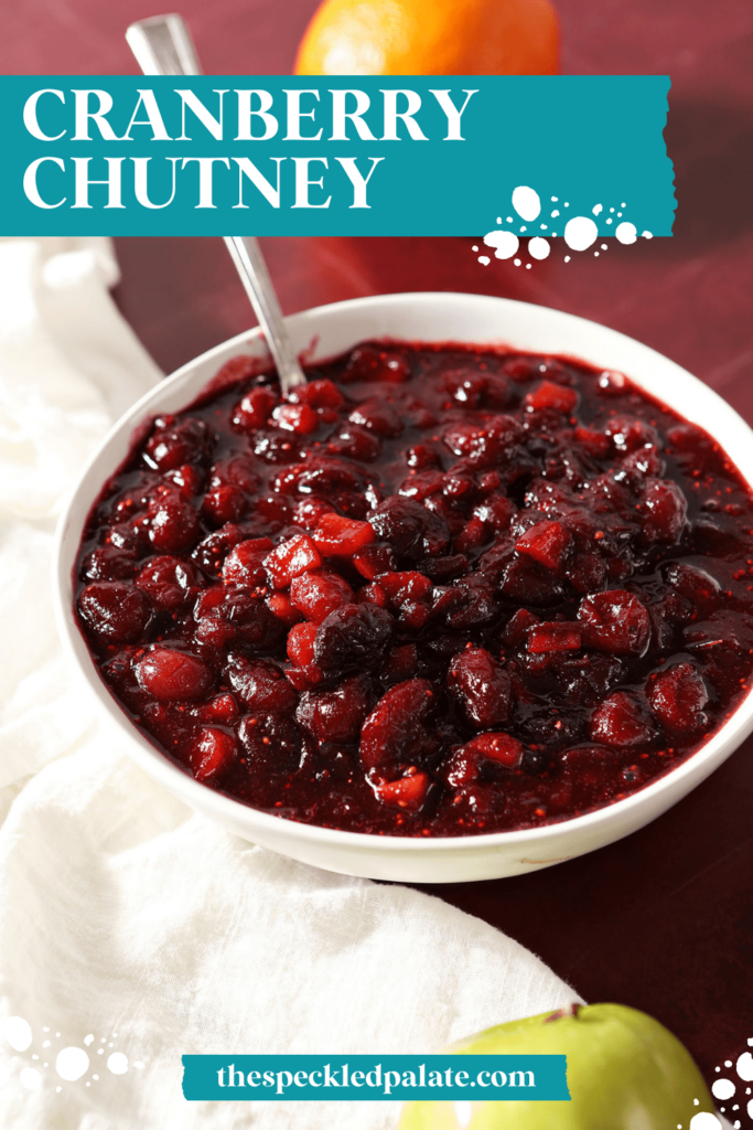 A white bowl of chutney with a spoon in it on a red countertop with a white towel with the text Cranberry Chutney