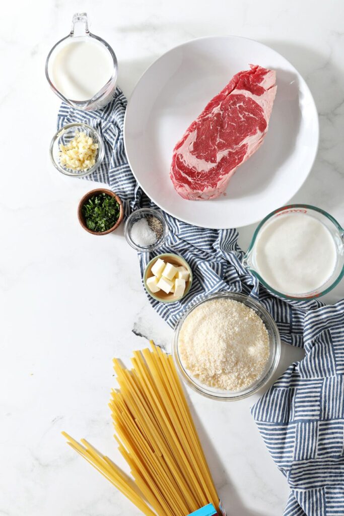 Ingredients to make steak Alfredo on a marble surface in bowls