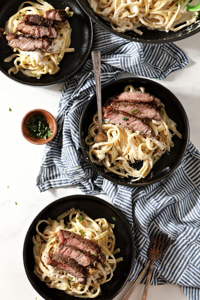 Three bowls of pasta in a cream sauce with steak from above