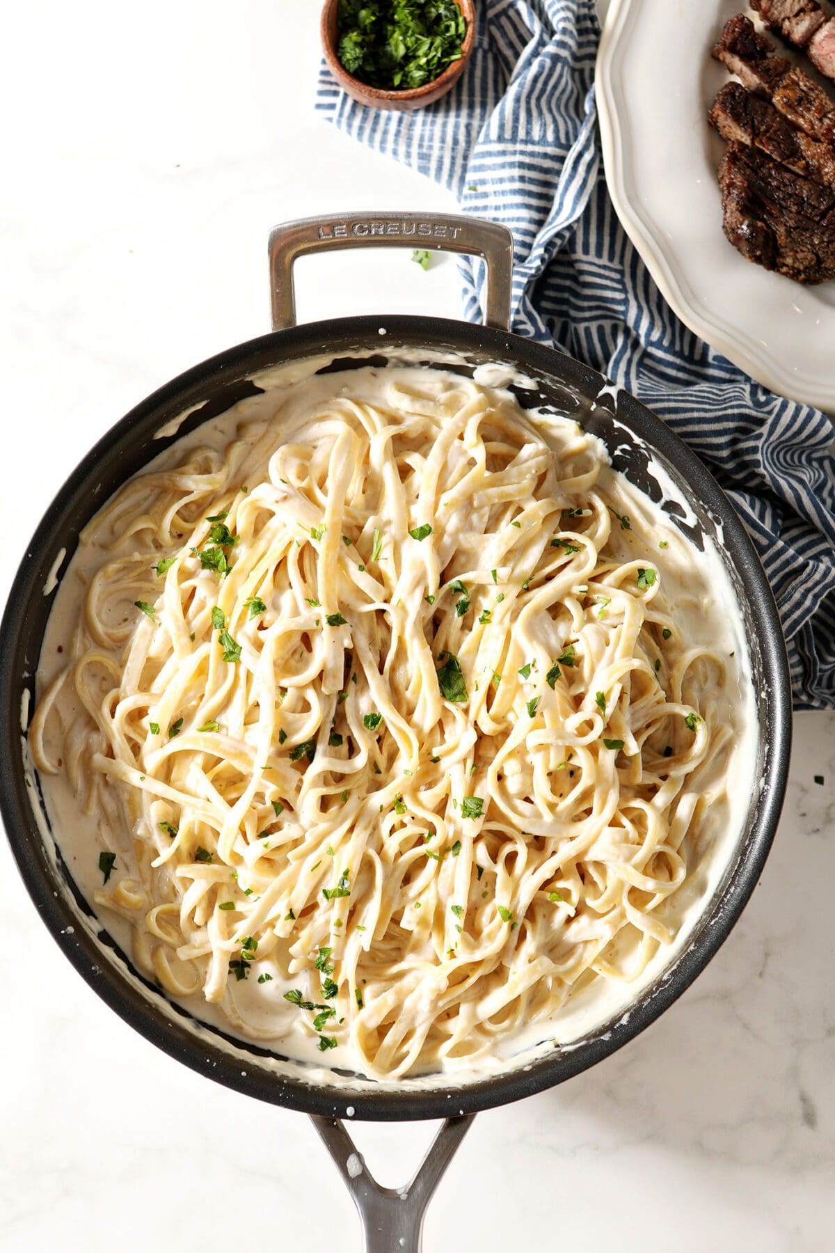 A skillet of fettuccine tossed in Alfredo sauce garnished with parsley