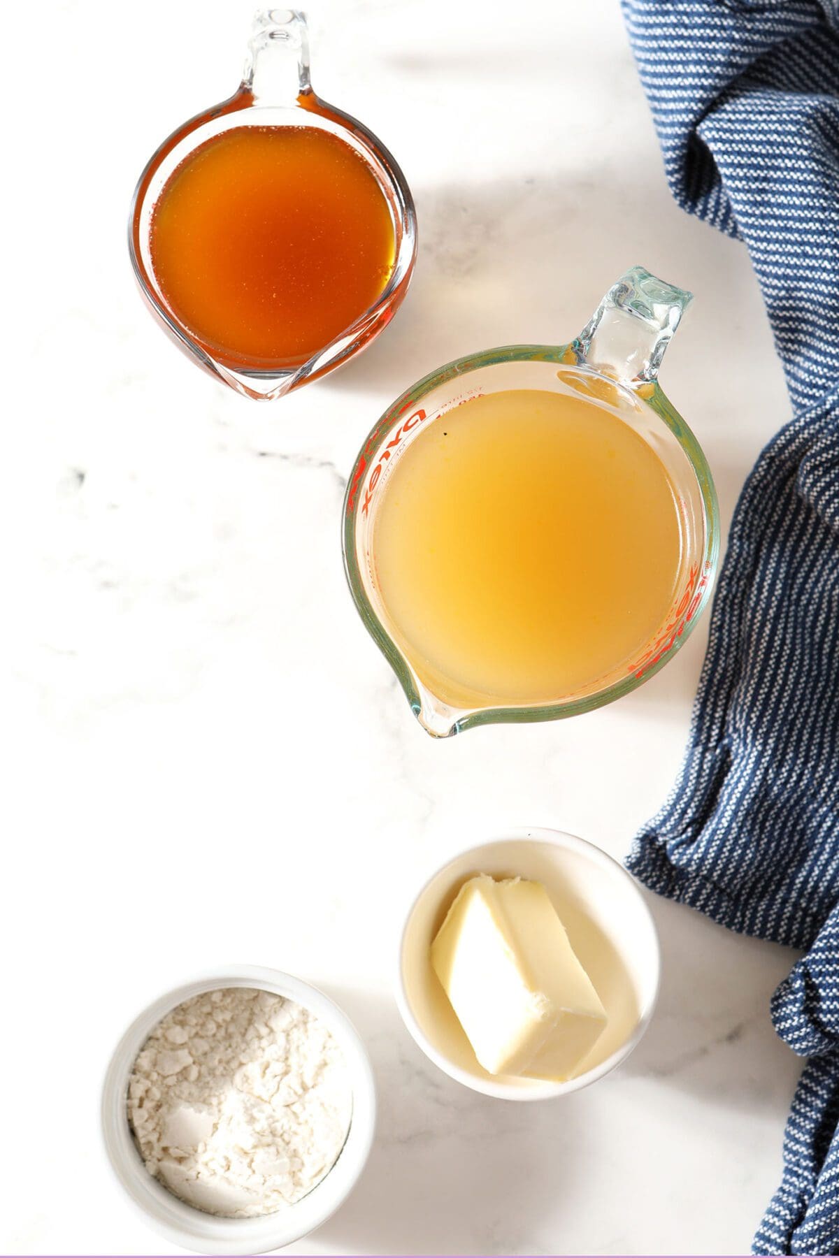 Ingredients to make turkey gravy in bowls and measuring cups on marble with a dark blue towel