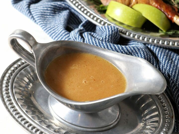 A gravy boat holds turkey gravy next to a platter of roasted turkey