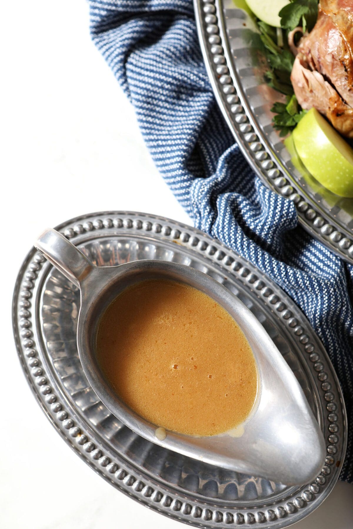 A silver gravy boat holds turkey gravy next to a platter of turkey
