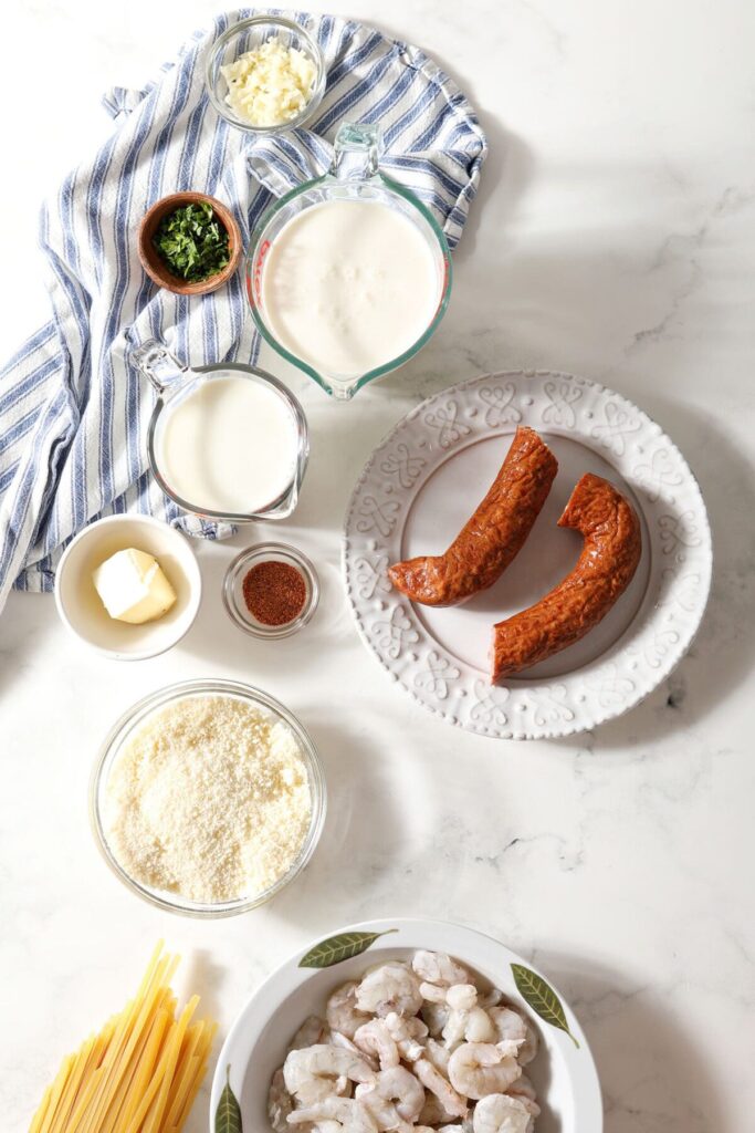 Ingredients to make Cajun Shrimp Alfredo on plates and bowls on marble