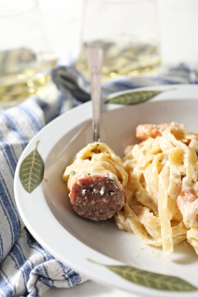 Close up of a fork spearing a sausage with noodles wrapped around it