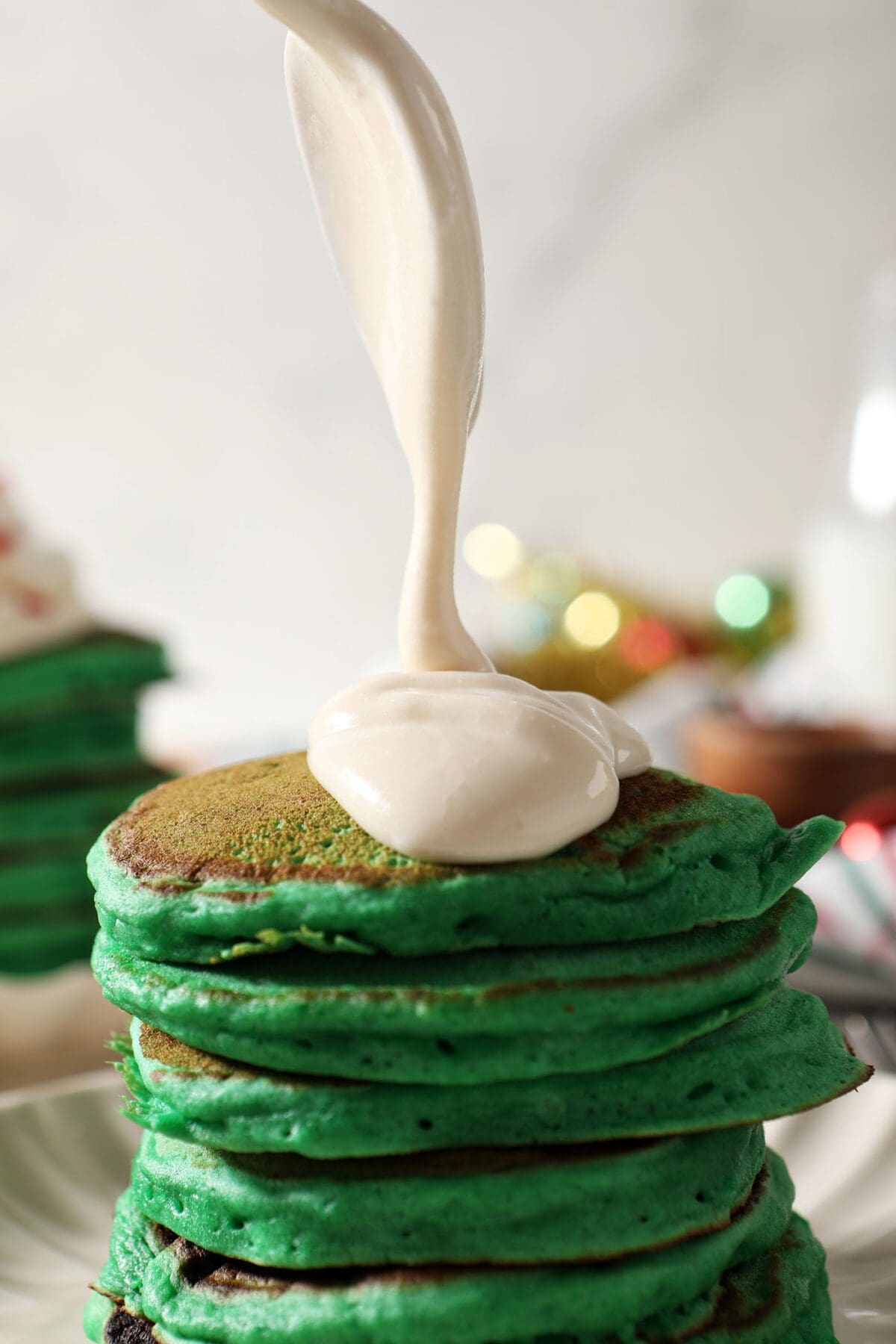 Cream cheese frosting drizzles onto a stack of green pancakes