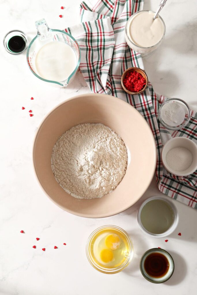 Ingredients to make green pancakes in bowls on a marble countertop with a green and red plaid towel