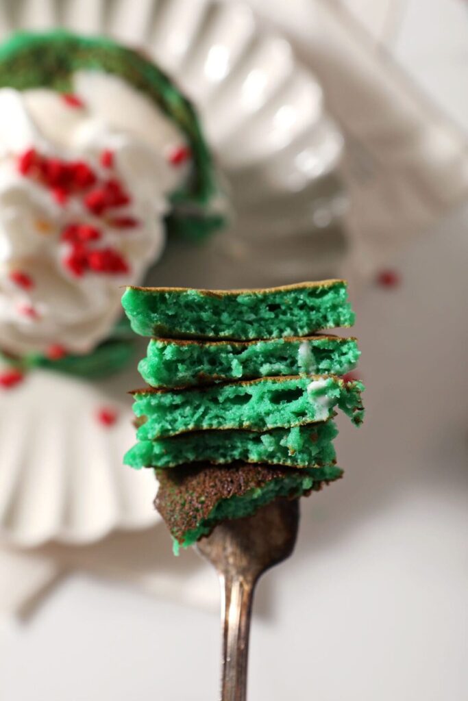 A fork holds a bite of stacked bright green pancakes above a plate of pancakes