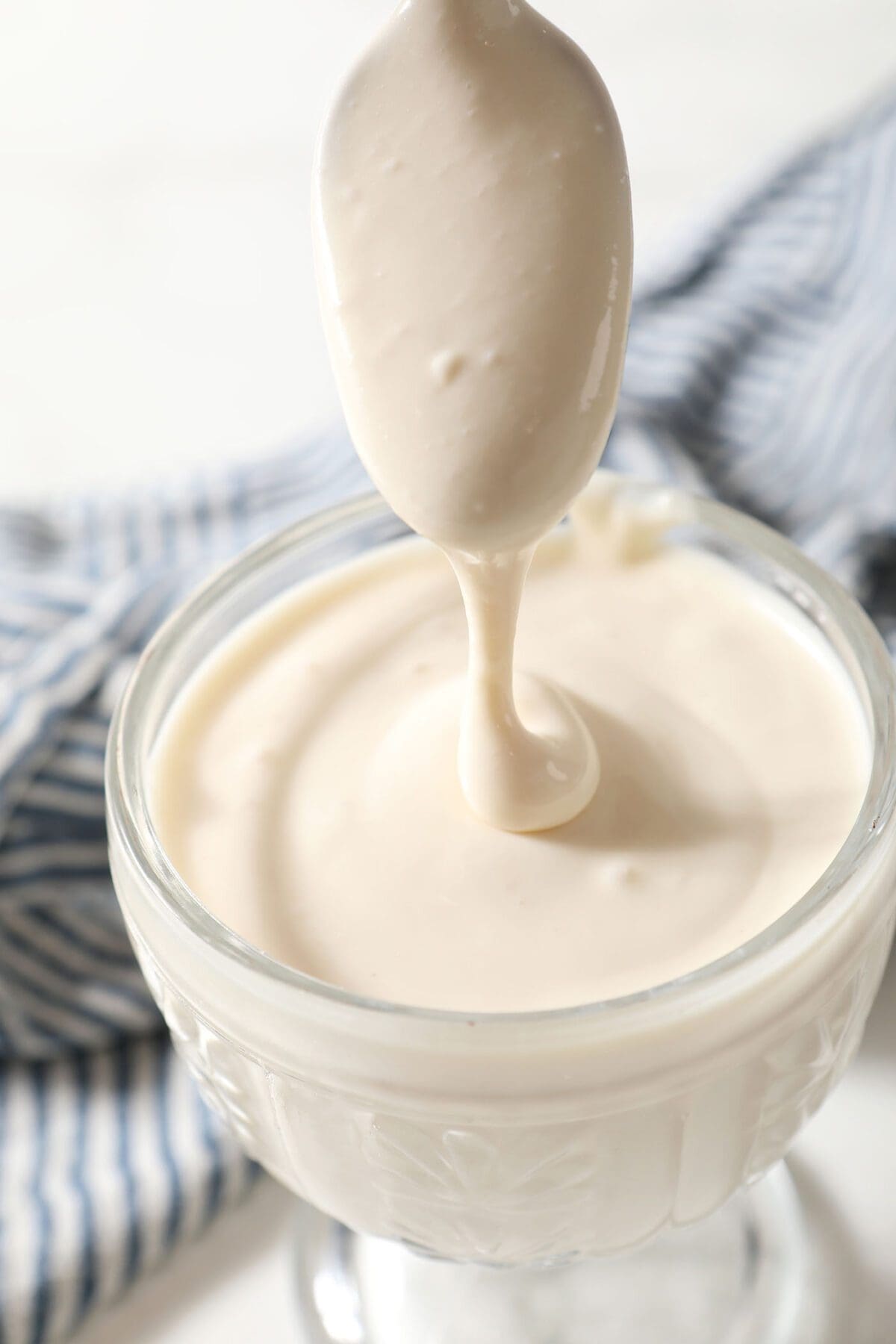 Cream cheese frosting on a spoon drizzles into a bowl