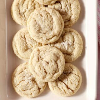 A rectangular platter stacked high with Drop Sugar Cookies on a pink countertop