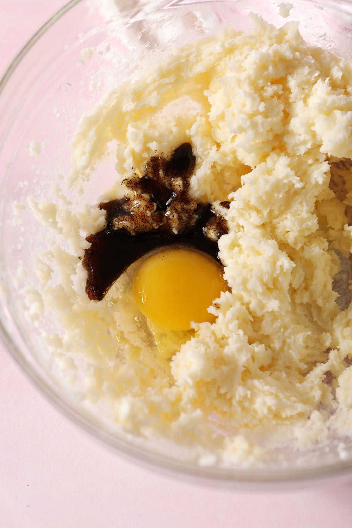 Close up of an egg and vanilla bean paste on top of creamed butter and sugars in a bowl