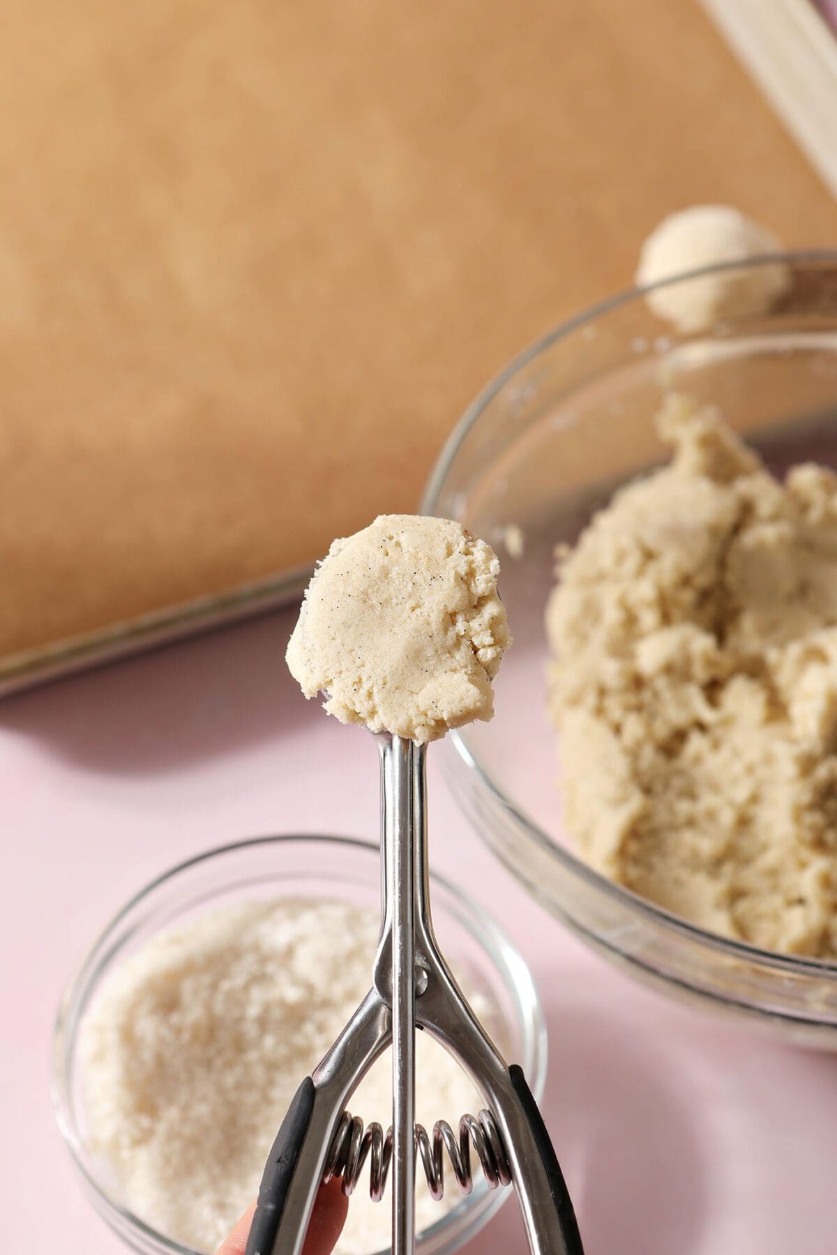 A cookie scoop holds cookie dough above a baking sheet lined with parchment